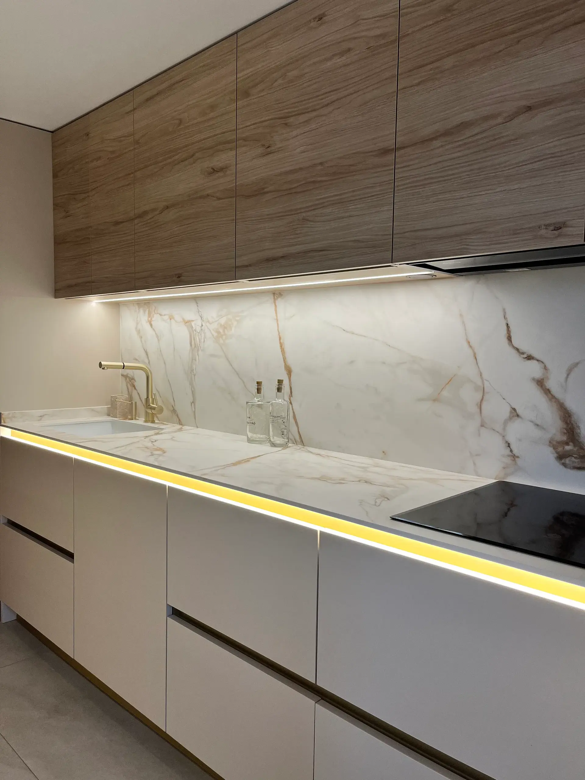 Cocina lineal en cachemir con gola, altos de roble y encimera y frente de porcelánico Calacatta Gold