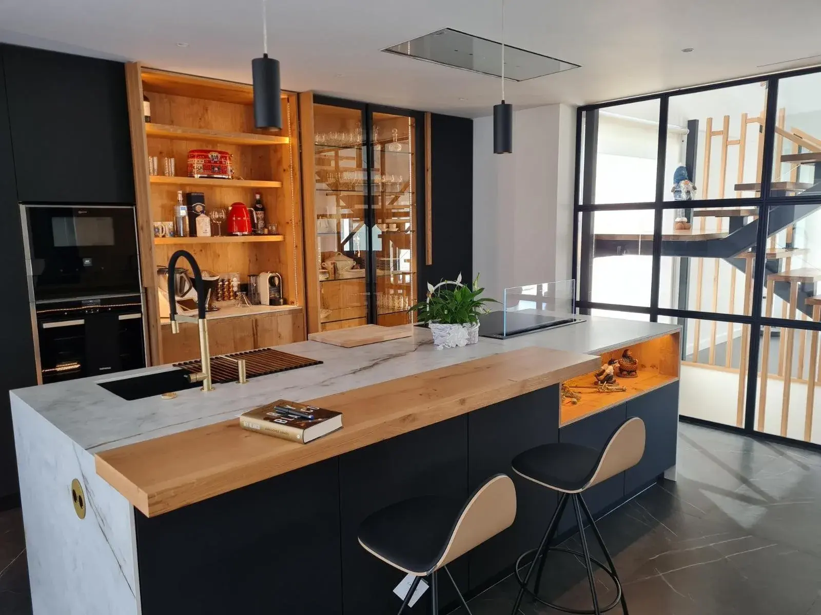 Cocina negra con isla de mármol, barra de roble y vitrina iluminada