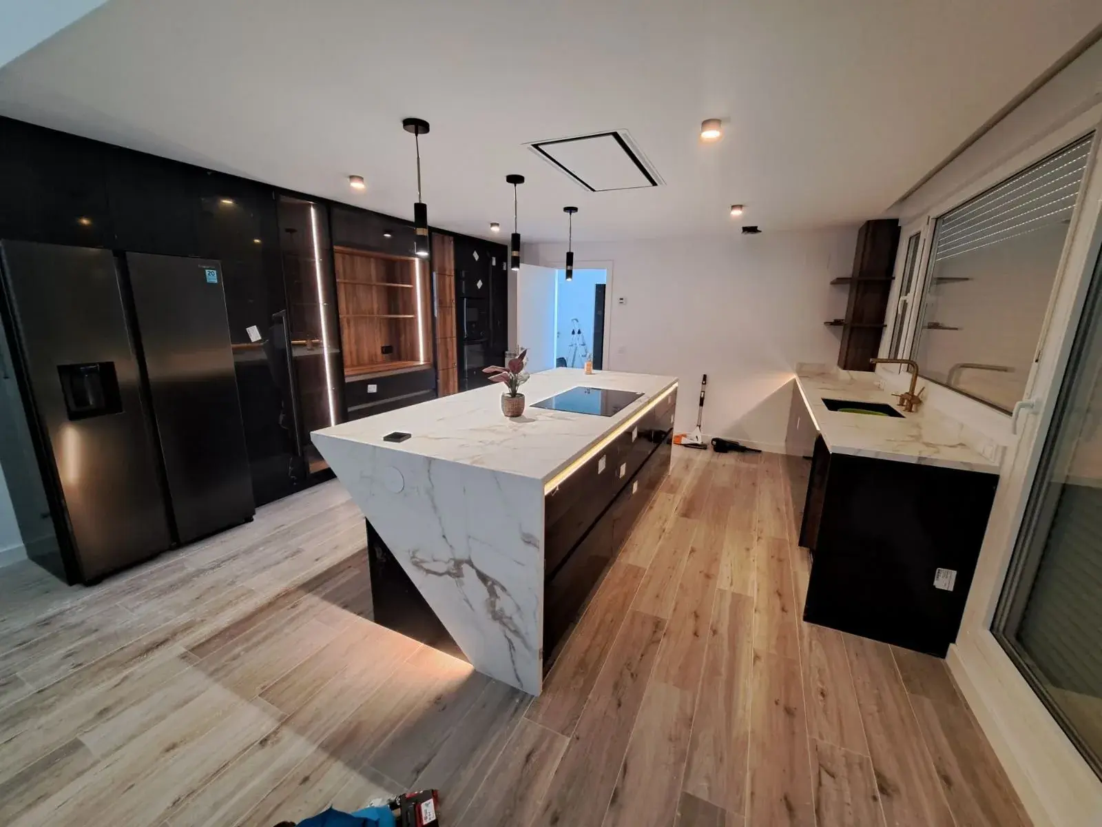 Cocina negra con isla de mármol blanco y suelo de madera