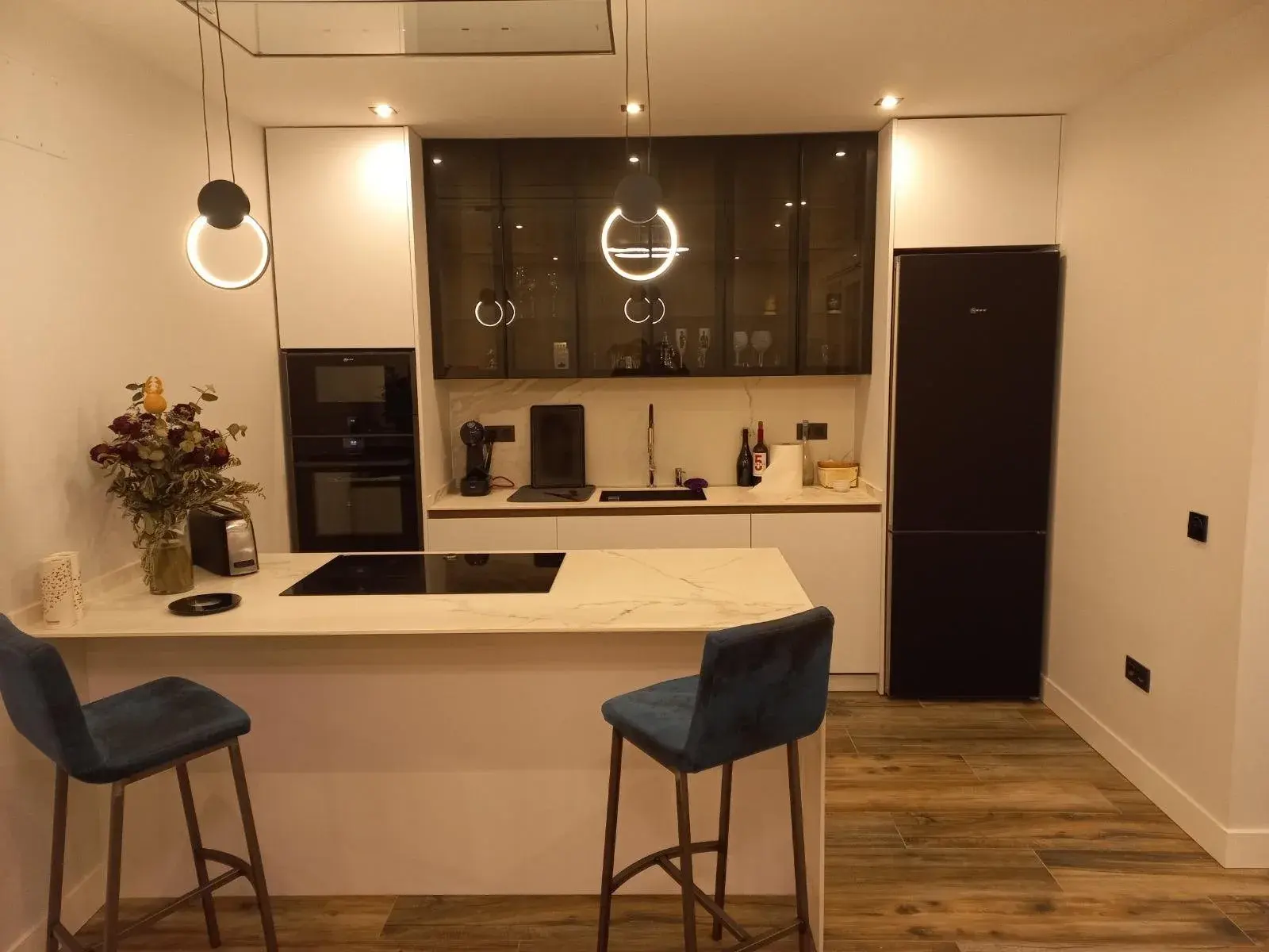 Cocina blanca con barra de mármol, vitrinas de aluminio y lámparas circulares