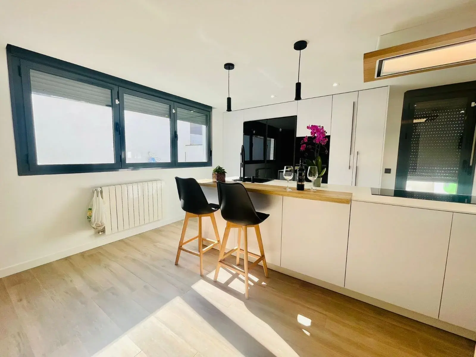 Cocina blanca con península de roble y taburetes, junto a la ventana