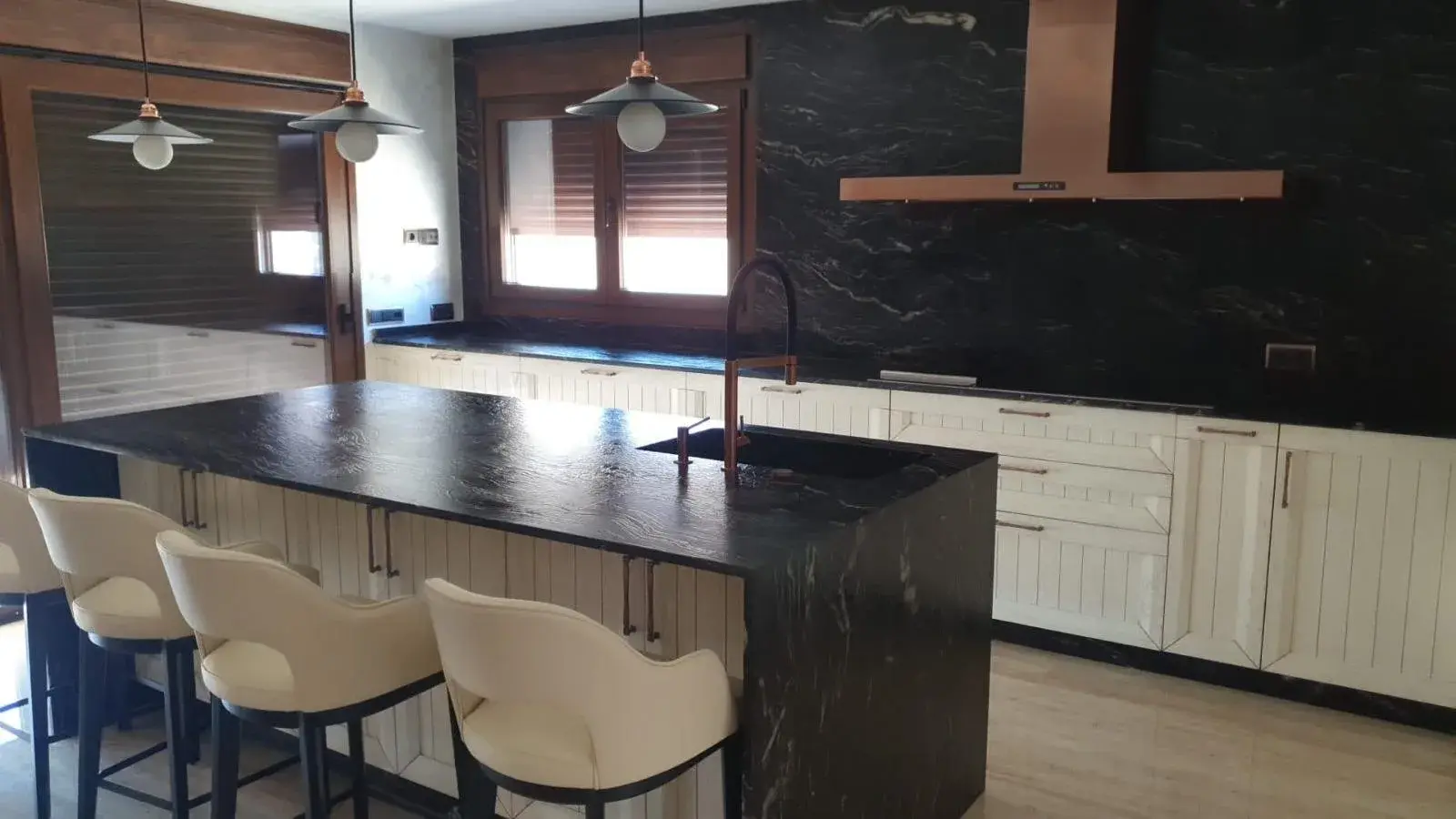 Cocina blanca de listones con isla de piedra negra y campana de cobre