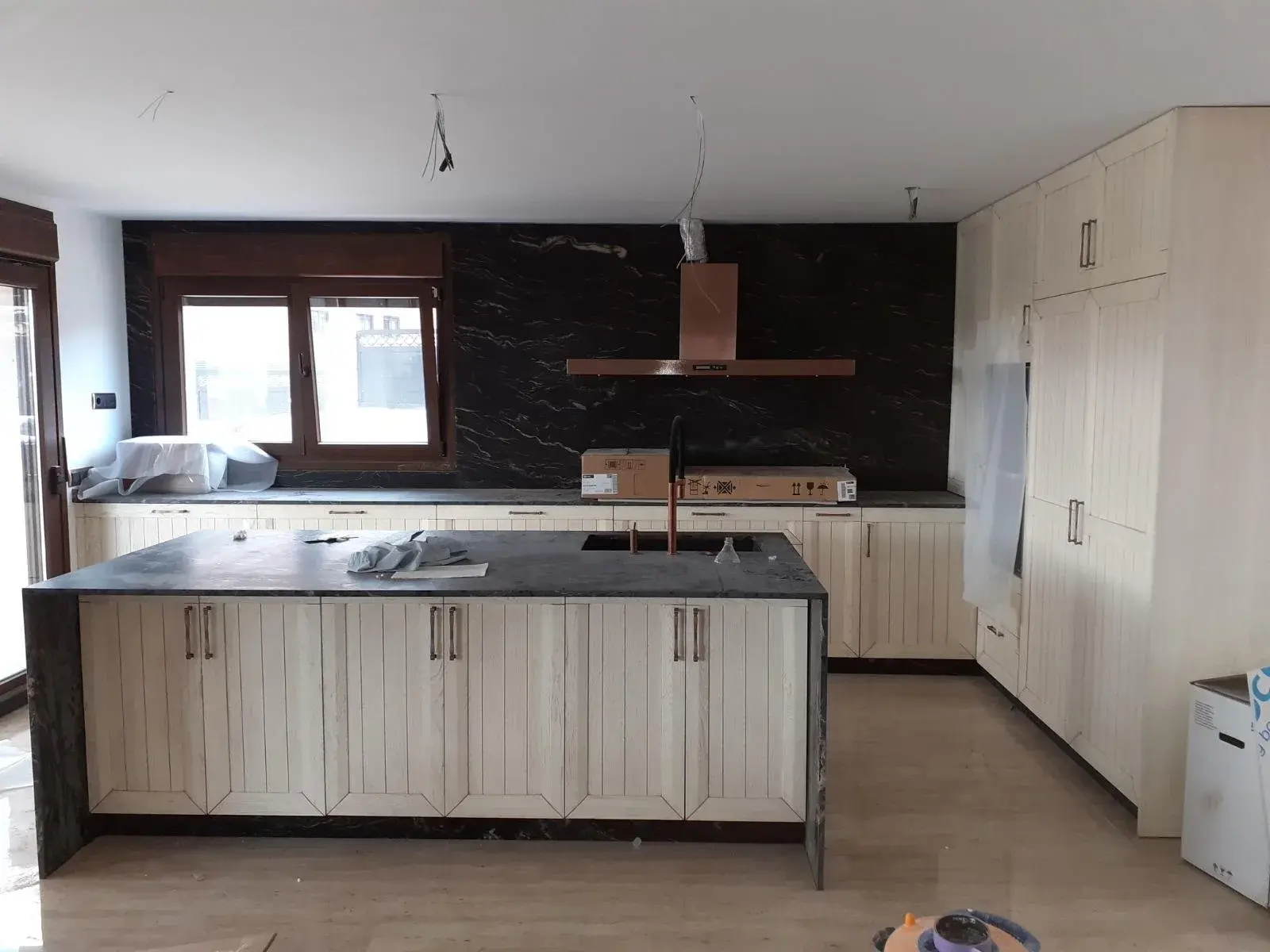 Cocina blanca de listones con isla de piedra negra durante el montaje